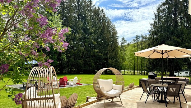 A wooden deck with outdoor furniture, including chairs and a table, surrounded by a lush garden and trees.