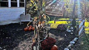 A sign for The Hancock Village Inn in Berkshire, Massachusetts, with a rustic outdoor setting including a wooden bench, pumpkins, and a corn decoration.