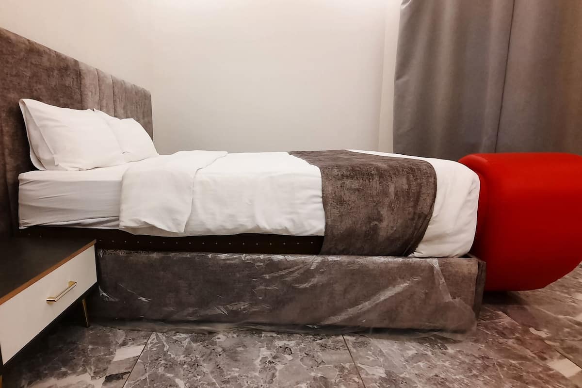 A modern hotel room with a bed, a nightstand, and a red ottoman.