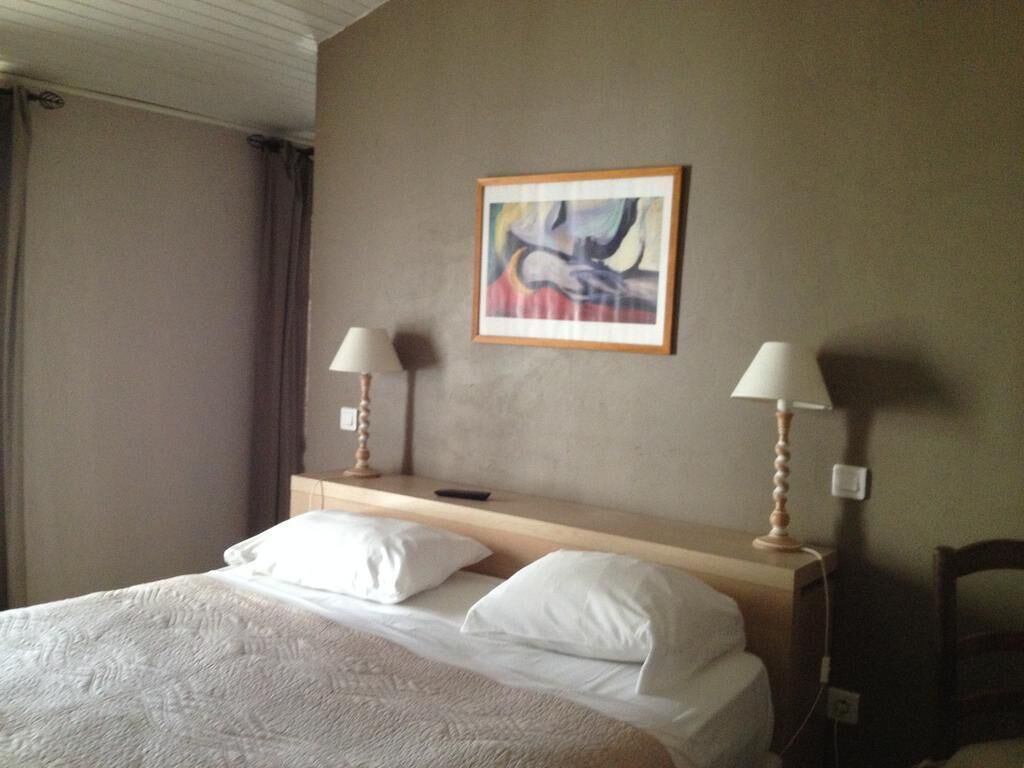 A hotel room with a bed, two bedside lamps, a framed abstract painting, and a window with curtains.