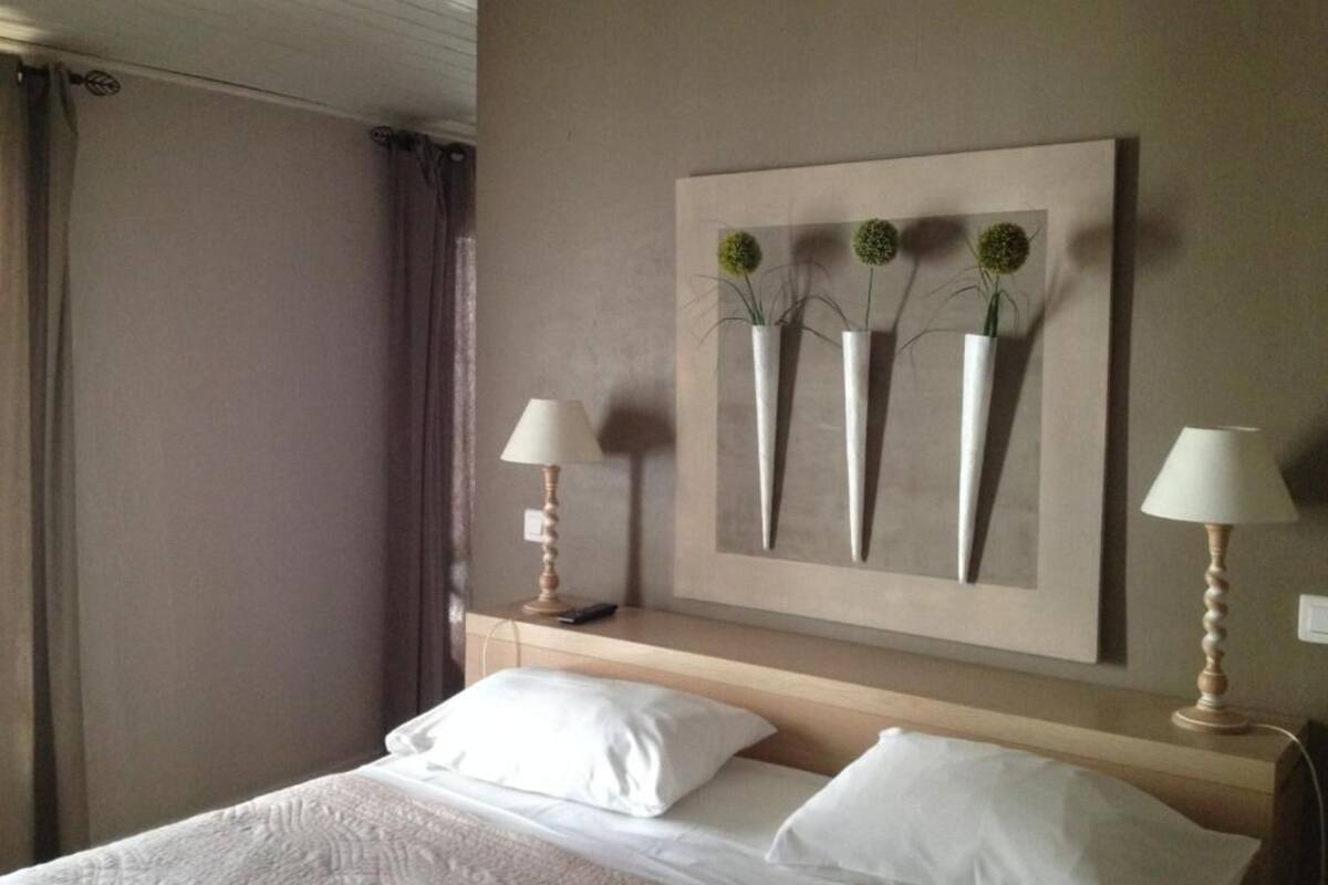 Une chambre d’hôtel avec un lit, deux lampes de chevet, une œuvre d’art accrochée au mur et une fenêtre avec des rideaux.