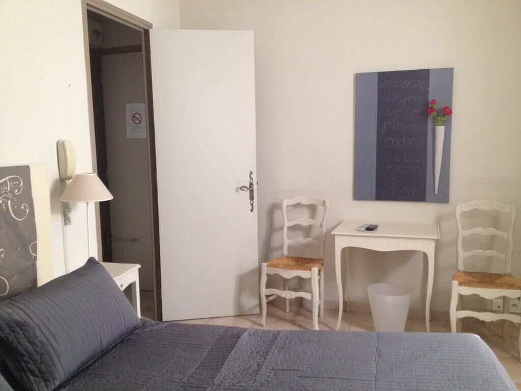 A bedroom with a bed, a desk, two chairs, a door, and a wall-mounted artwork.