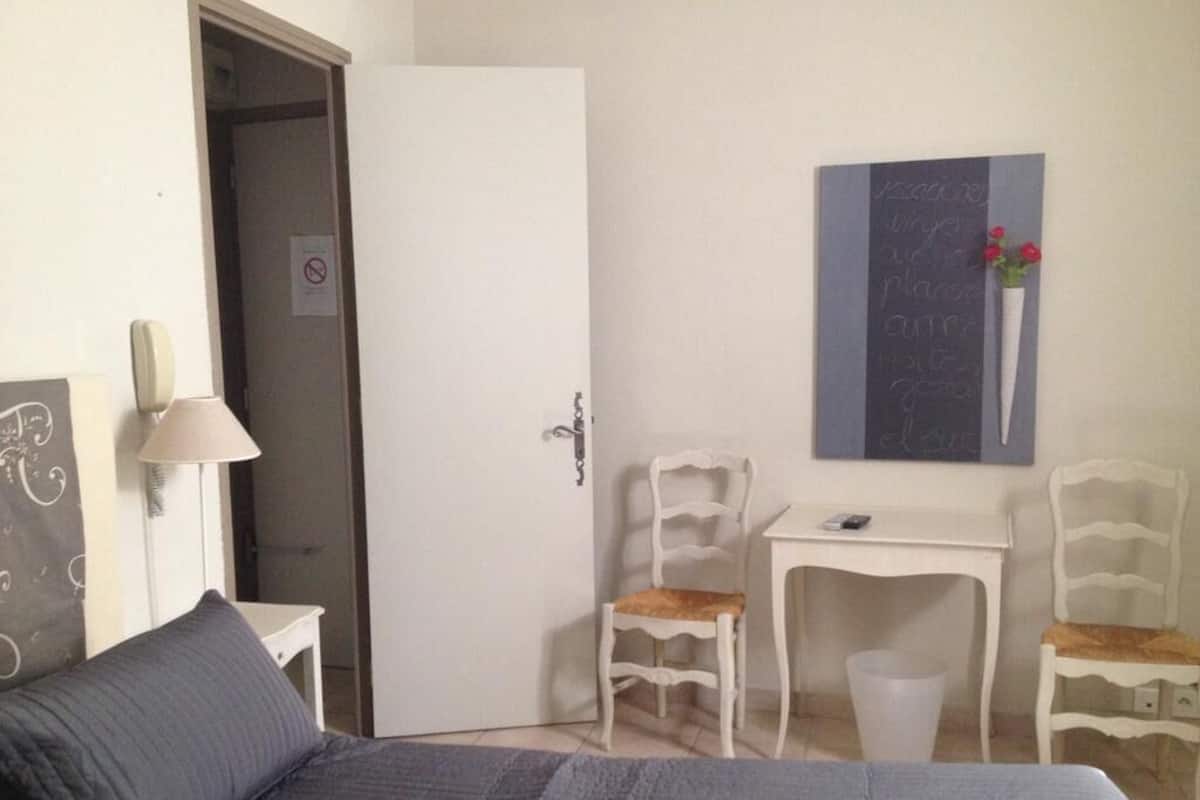 Une chambre à coucher comprenant un lit, un bureau, deux chaises, une porte et une œuvre d’art accrochée au mur.