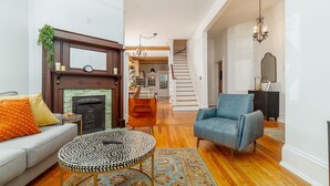 Ein Wohnzimmer mit Kamin, einer Couch, einem blauen Sessel, einem runden Couchtisch und einer Treppe zu einem anderen Raum.