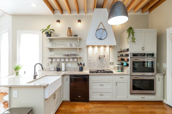 A modern kitchen with white cabinetry, a granite countertop, a dishwasher, a stove, and an oven.
