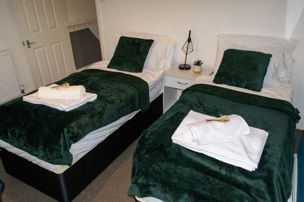 Two twin beds with green bedding, white pillows, and folded towels on each bed. - 2 bed house Sedley Street Liverpool (Liverpool)