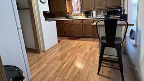 Une cuisine compacte avec des meubles en bois, un réfrigérateur blanc, une horloge et un coin repas avec une chaise.