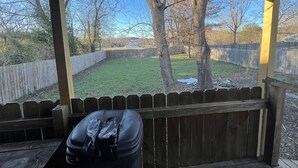 Un patio couvert donnant sur un jardin, une clôture en bois et des arbres.