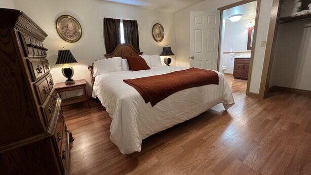 Une chambre à coucher avec un grand lit, une commode en bois, deux lampes de chevet et un ventilateur de plafond.
