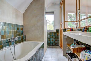 A bathroom with a bathtub, tiled walls, a window, and a sink with toiletries. - Villa Dremmwel - Five Bedroom House, Sleeps 10 (Île-aux-Moines)