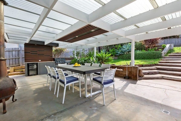 An outdoor patio with a table and chairs, a grill, and a wooden deck.