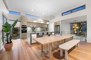 A modern kitchen with a central island, a dining area with a bench, and large windows providing natural light. - Waterline Ocean Front Luxury  Bells Beach (Jan Juc)