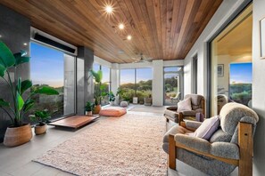 Un interior moderno con techo de madera, ventanas amplias y una zona de estar con alfombra y plantas.