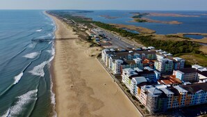 Vista aerea di un hotel sulla costa con diversi edifici colorati, una spiaggia e un molo che si estende nell'oceano.