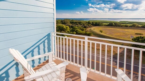 Un balcone con sedie Adirondack bianche e vista su una strada e campi.