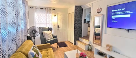 A modern living room with a yellow sofa, a white coffee table, and a flat-screen TV mounted on the wall.