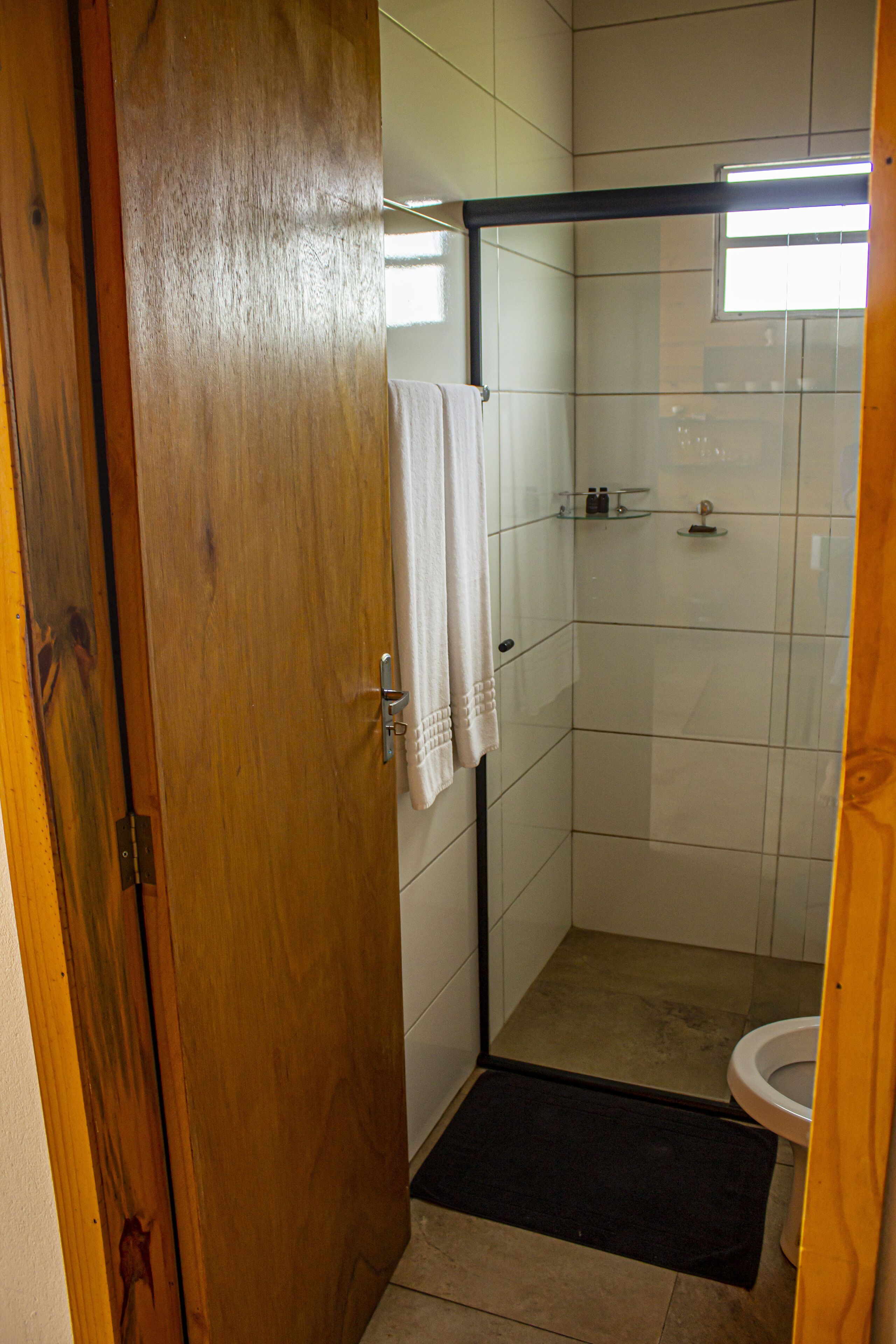Pieni, laatoitettu kylpyhuone, jossa on suihku, wc ja puuovi.