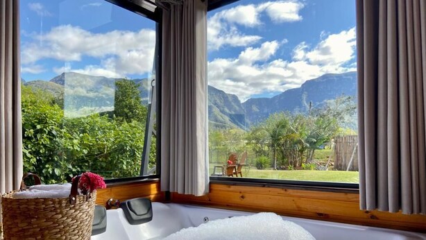Quarto com uma janela grande, piso de madeira, banheira cheia de espuma e um cesto de vime com flores.