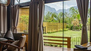 Quarto com cama grande, móveis de madeira e vista para um jardim e montanhas.