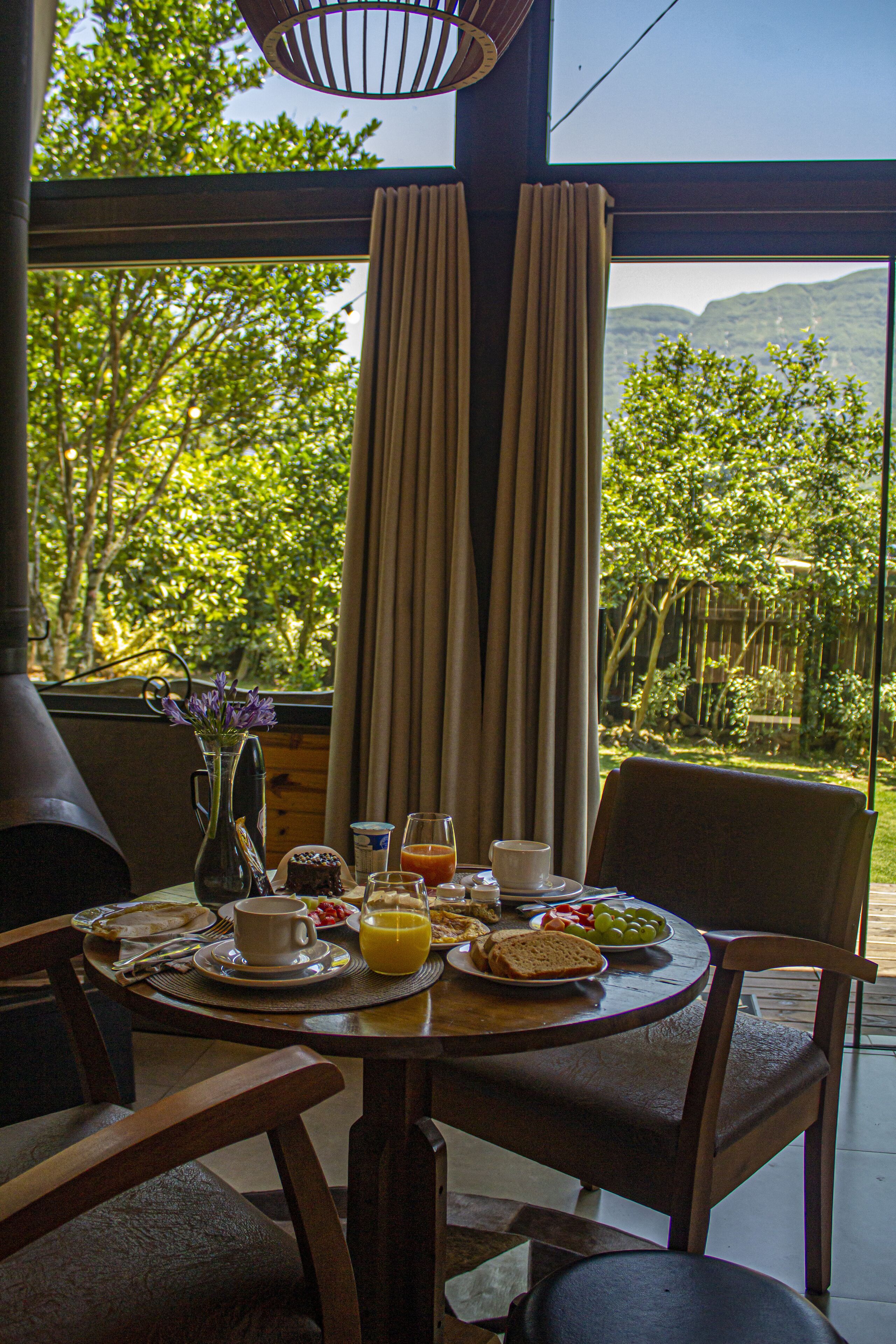 A breakfast table with a view of a lush garden and mountains.
