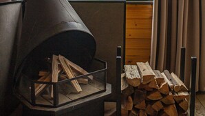 A wood stove with logs, a stack of firewood, and a view of a mountainous landscape through a window. - Cabanas Jardim dos Canyons (Praia Grande)