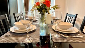 A dining table set with white plates, bowls, and wine glasses, flanked by chairs. A vase with flowers is centered on the table.