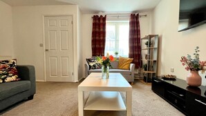A living room with a white table, grey sofa, and a TV on the wall.