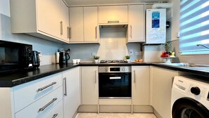 A compact kitchen with white cabinets, a black stove, a microwave, a washing machine, and a small sink.
