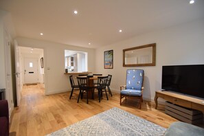 A modern living room with a dining area, wooden flooring, a TV, and a patterned rug. - Southbank family-friendly holiday cottage in Rye, close to the centre (Rye)