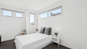 A bedroom with a bed, two bedside tables, a nightstand, a radiator, and three windows. - Eastern Views - Modern living with pool and table tennis. (Portarlington)