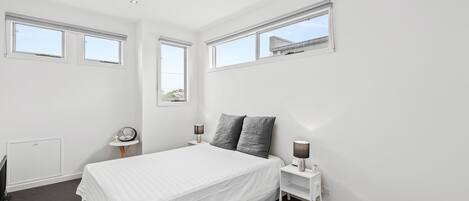 Una camera da letto con un letto, due comodini, un tavolo di appoggio, un termosifone e tre finestre.
