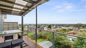 A balcony with a glass table and chairs, overlooking a residential area with houses and a clear sky. - Eastern Views - Modern living with pool and table tennis. (Portarlington)