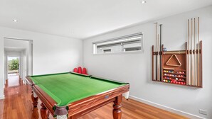 A pool table with a green felt surface, a red seating area, and a wooden rack holding pool cues and balls. - Eastern Views - Modern living with pool and table tennis. (Portarlington)