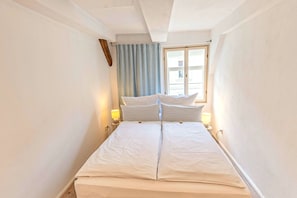 Ein Schlafzimmer mit einem Bett, zwei Nachttischlampen, einem Fenster mit Vorhängen und einem Holzbalken an der Decke.