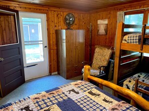 A cabin-style room with a bunk bed, a wooden wardrobe, a chair, and a fan.