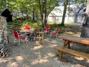 A rustic outdoor seating area with a fire pit, red chairs, and a wooden table.