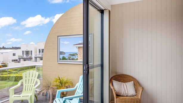 Un balcon avec deux chaises, un fauteuil en osier et une vue sur un bâtiment situé sur la côte.