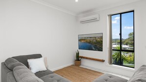 Un salon moderne avec un canapé gris, une grande fenêtre donnant sur une zone côtière et un climatiseur fixé au mur.