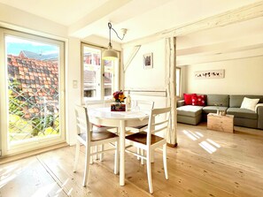 A dining area with a white table and chairs, a hanging light fixture, and a view of a red-roofed building through a window.