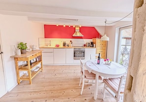 Une cuisine compacte avec un mur d’accent rouge, un plancher en bois et un coin repas comprenant une table blanche et des chaises à rayures.