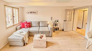 A cozy living room with a grey sectional sofa, a small ottoman, a coffee table, and a bookshelf. - ⭐️ heavenly courtyard - jewel from 1477 with parking, 70m², outdoor seating area (Quedlinburg)