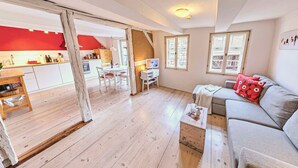 A cozy living room with a sofa, a coffee table, and a TV. There's a kitchen in the background with a red accent wall. - ⭐️ heavenly courtyard - jewel from 1477 with parking, 70m², outdoor seating area (Quedlinburg)