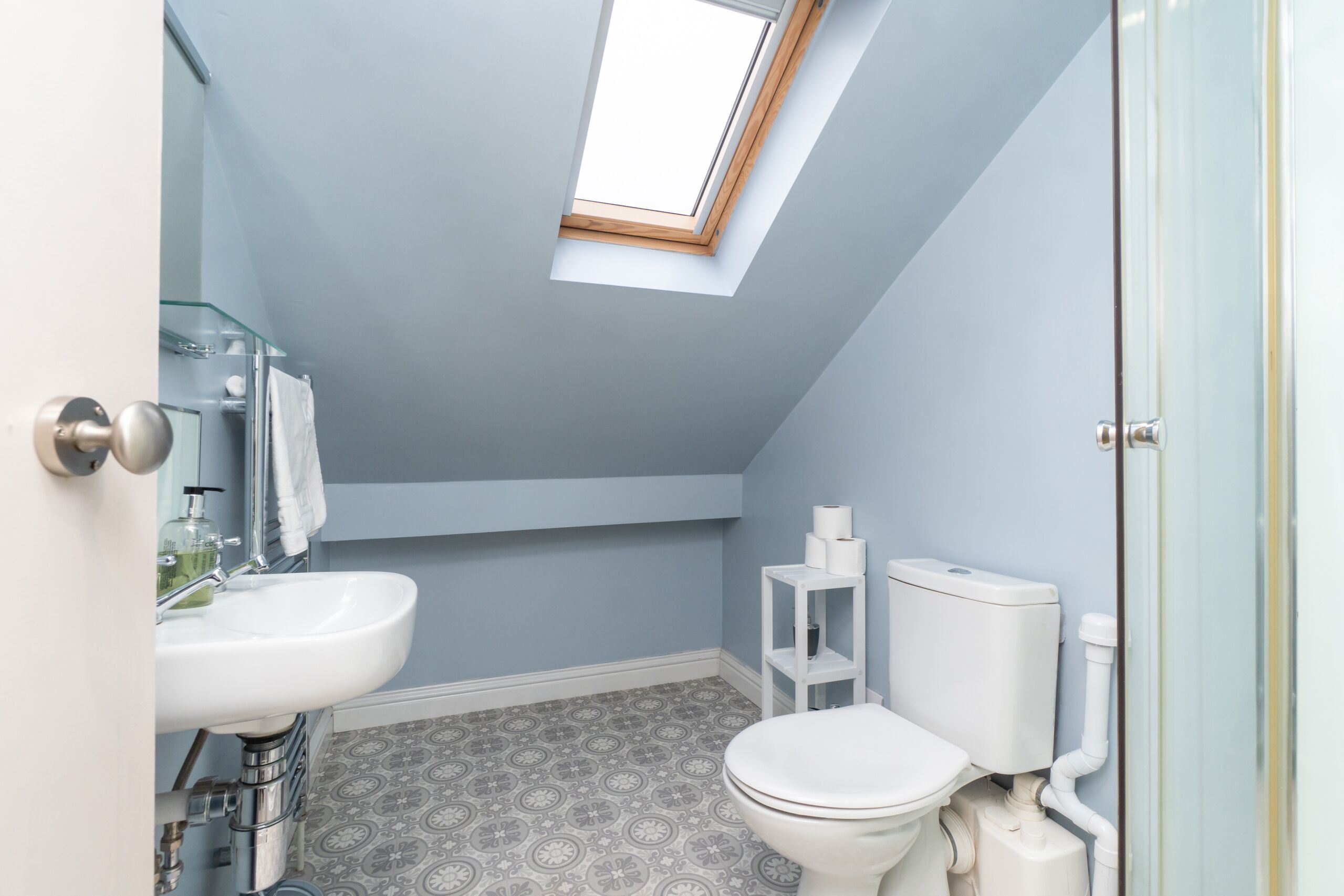 Un bagno piccolo e moderno con una finestra a lucernario, un lavandino bianco e un water.