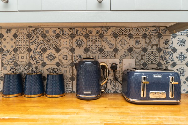 Una cocina con un tostador Breville, tres hervidores Breville y una cafetera Breville sobre una encimera de madera.
