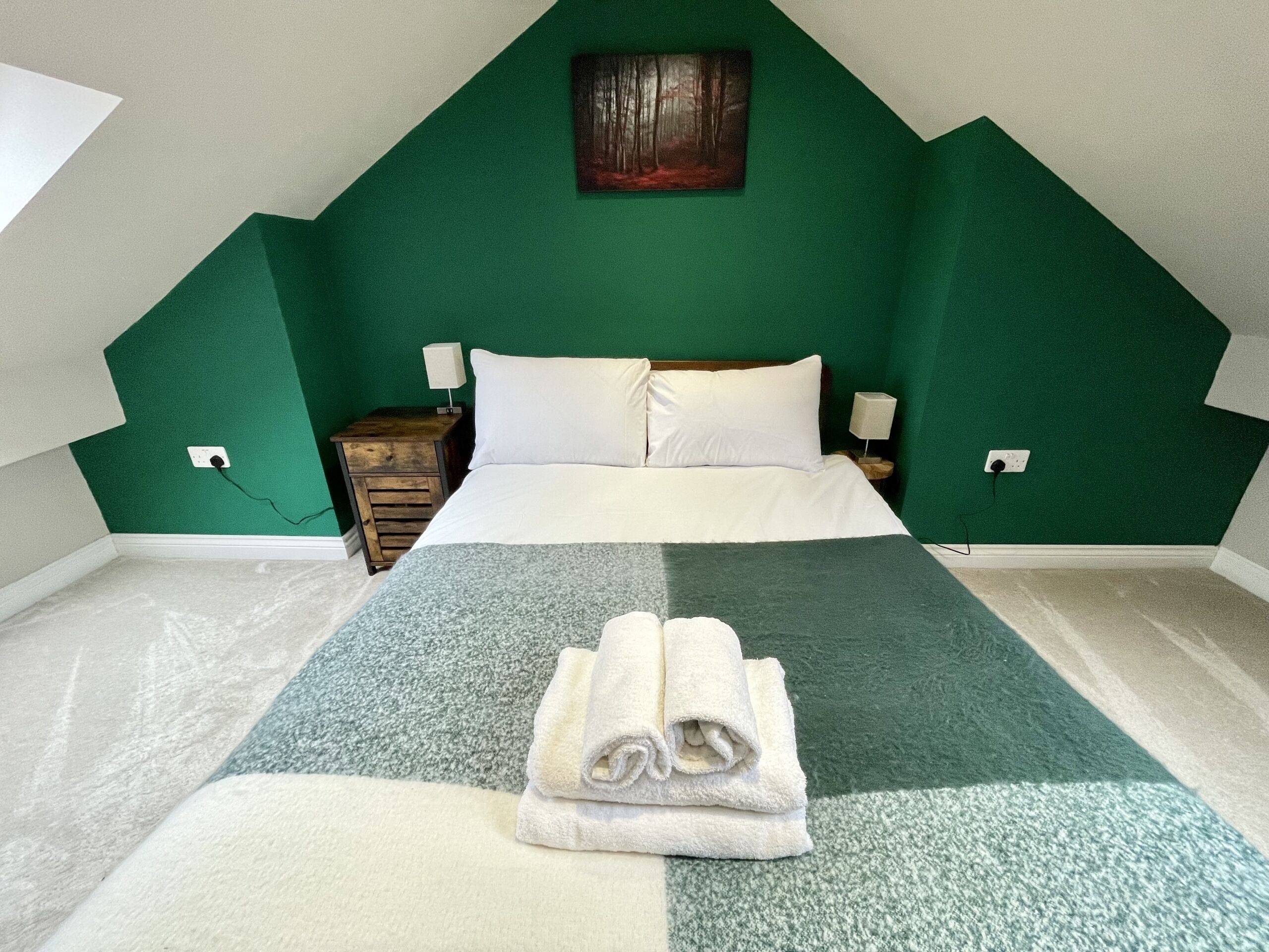 Un dormitorio con una cama, dos mesitas de noche, un cuadro colgado en la pared y una pared verde decorativa.