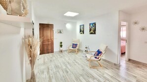 Una habitación amplia con suelo de madera, una estatua de Buda, dos sillas con cojines coloridos y una puerta que da a otra habitación.