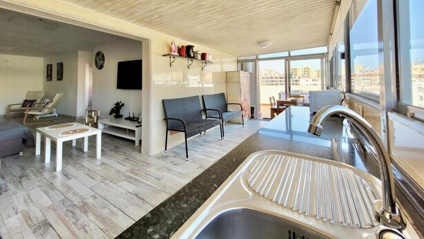 Un interior moderno con techo de madera, una zona de cocina con lavabo, un comedor y un área de estar con sofá y sillones.