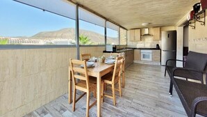 Un balcón amplio con mesa y sillas de madera, una zona de cocina y vistas a la montaña.