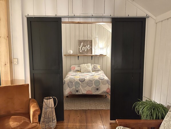 A bedroom with a bed, a wall-mounted shelf with decorative items, a wooden floor, and a sliding door.