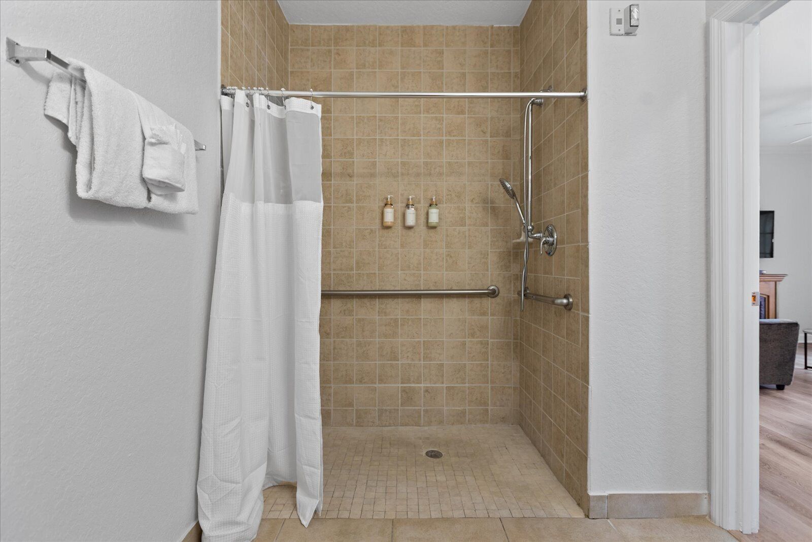 Un espace douche avec des carreaux de couleur beige, un rideau de douche blanc et une barre d’appui.